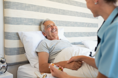 Cheerful senior man lying on bed receiving health care at home.