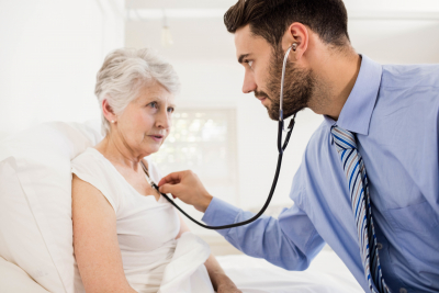 Home nurse listening to chest of patient with stethoscope at home